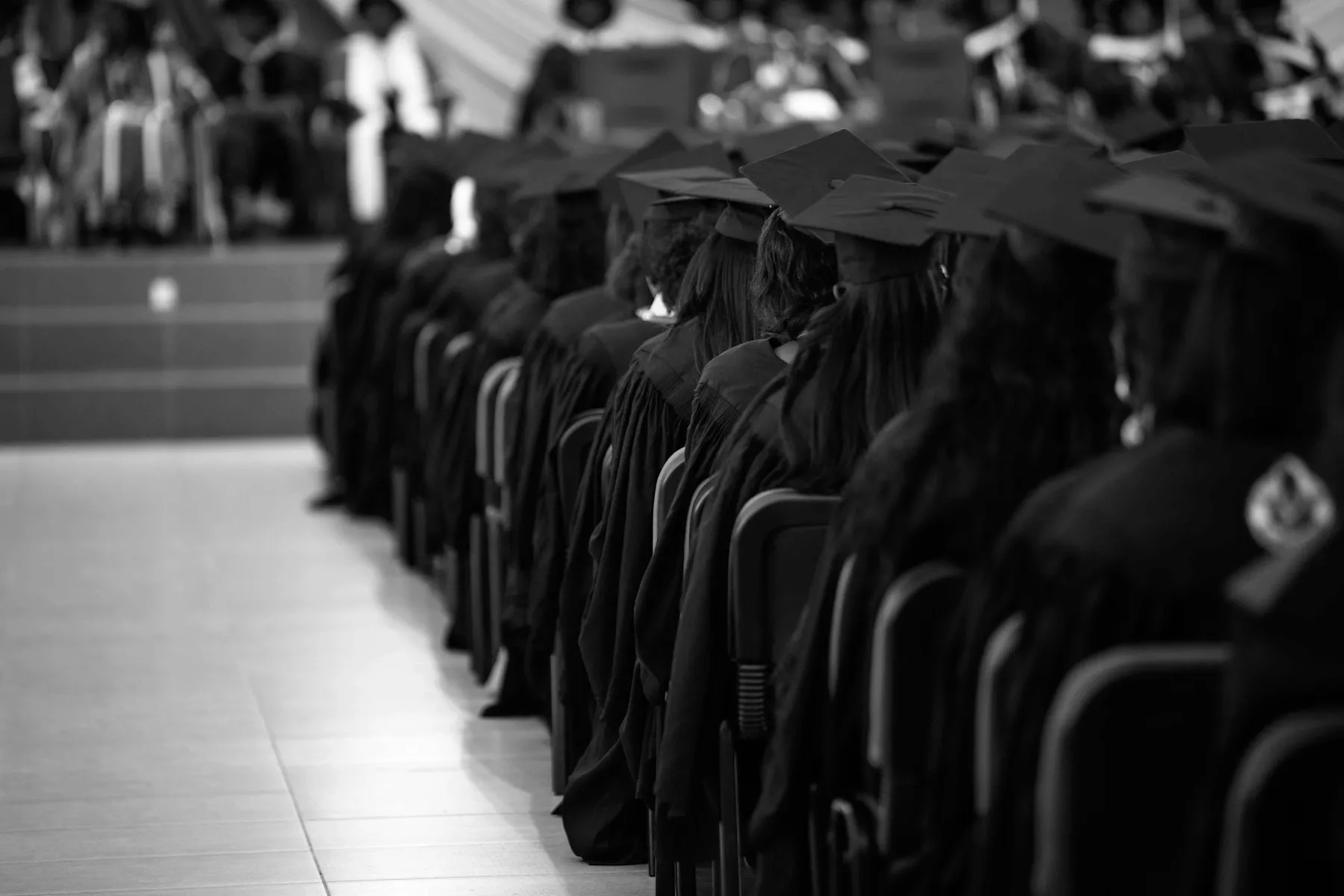 A row of graduates in caps and gowns seated at a ceremony, black and white