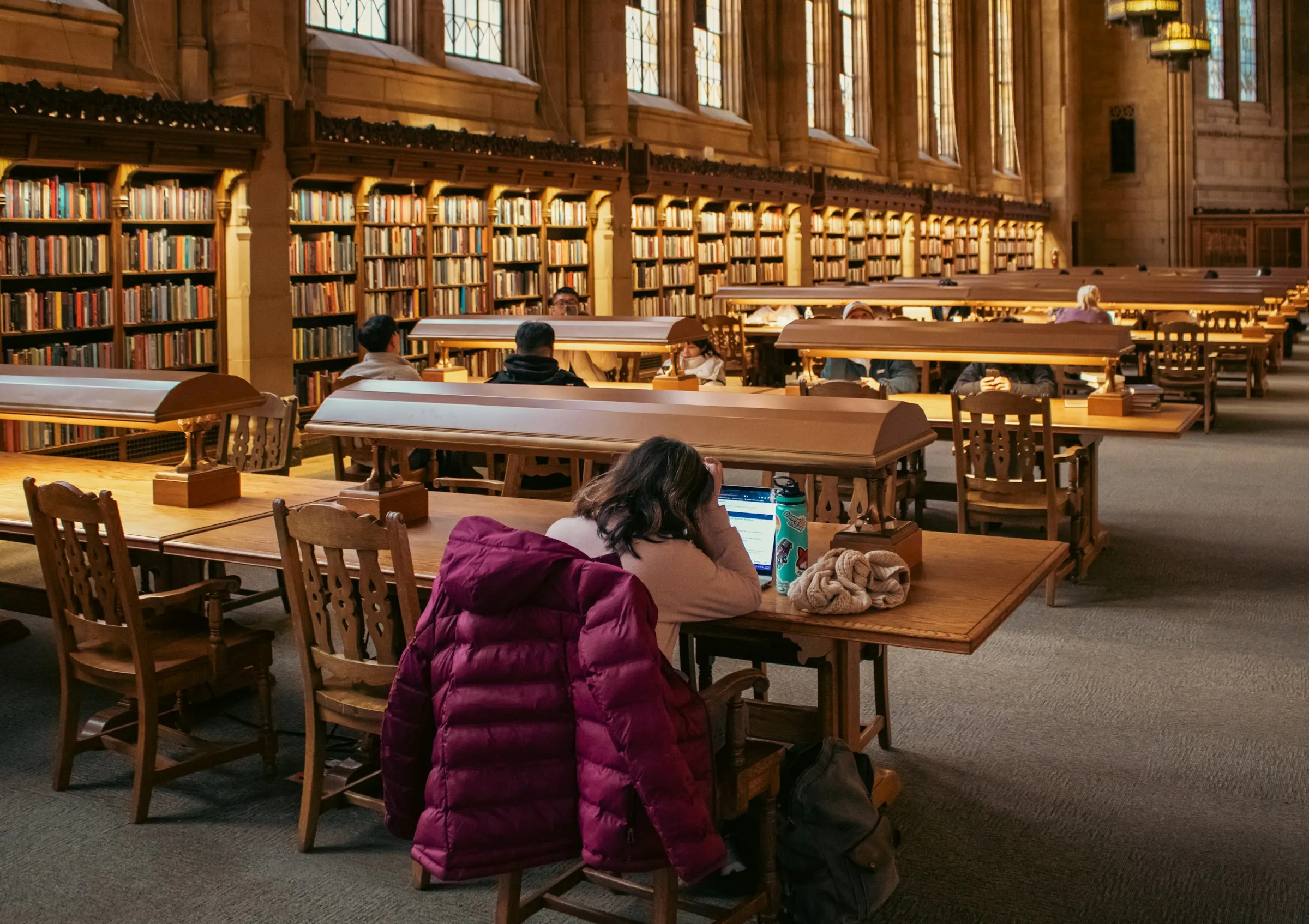A student studying at a table in a grand wood-panelled university library